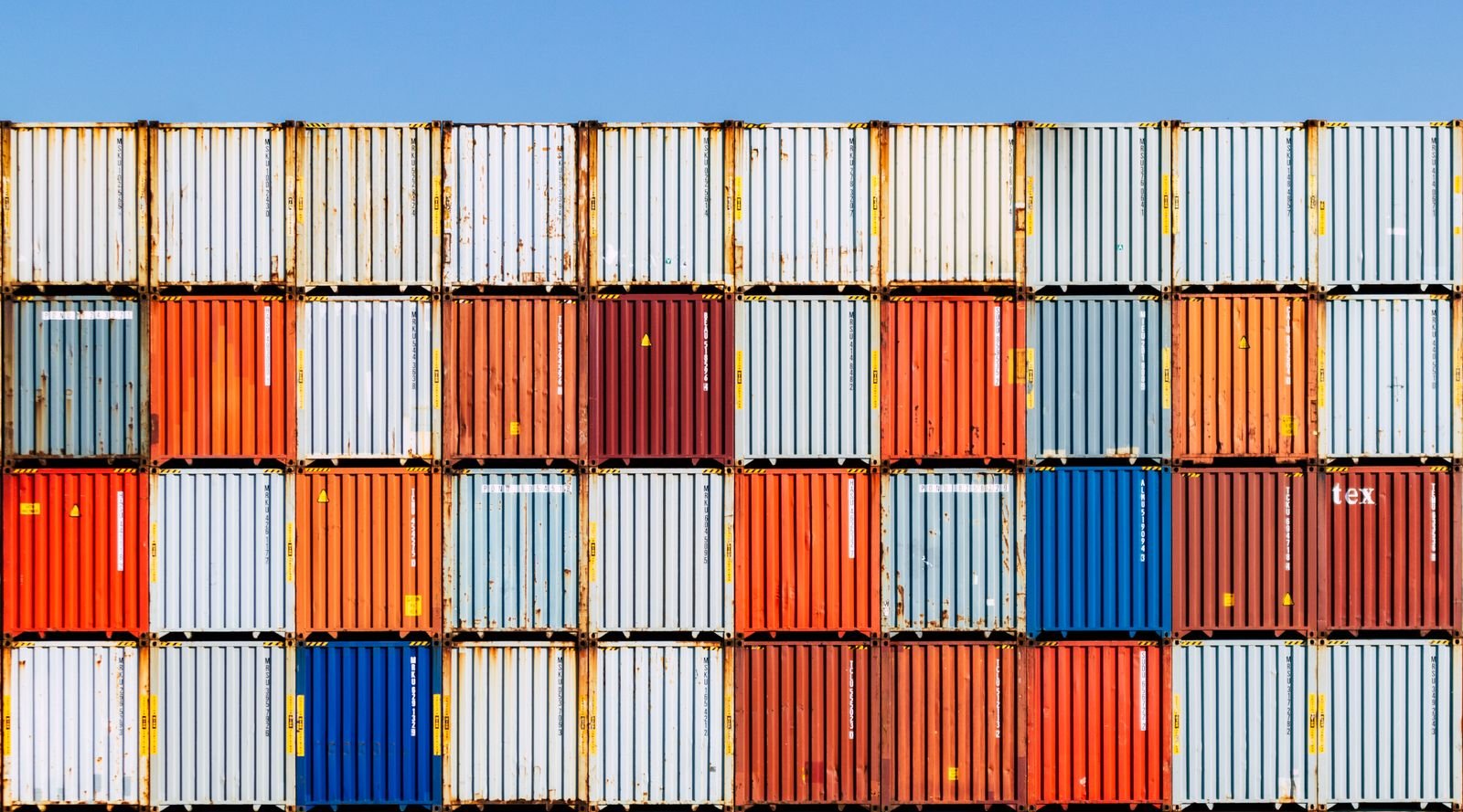 Colorful stacked shipping containers against a vibrant blue sky, conveying global trade and logistics