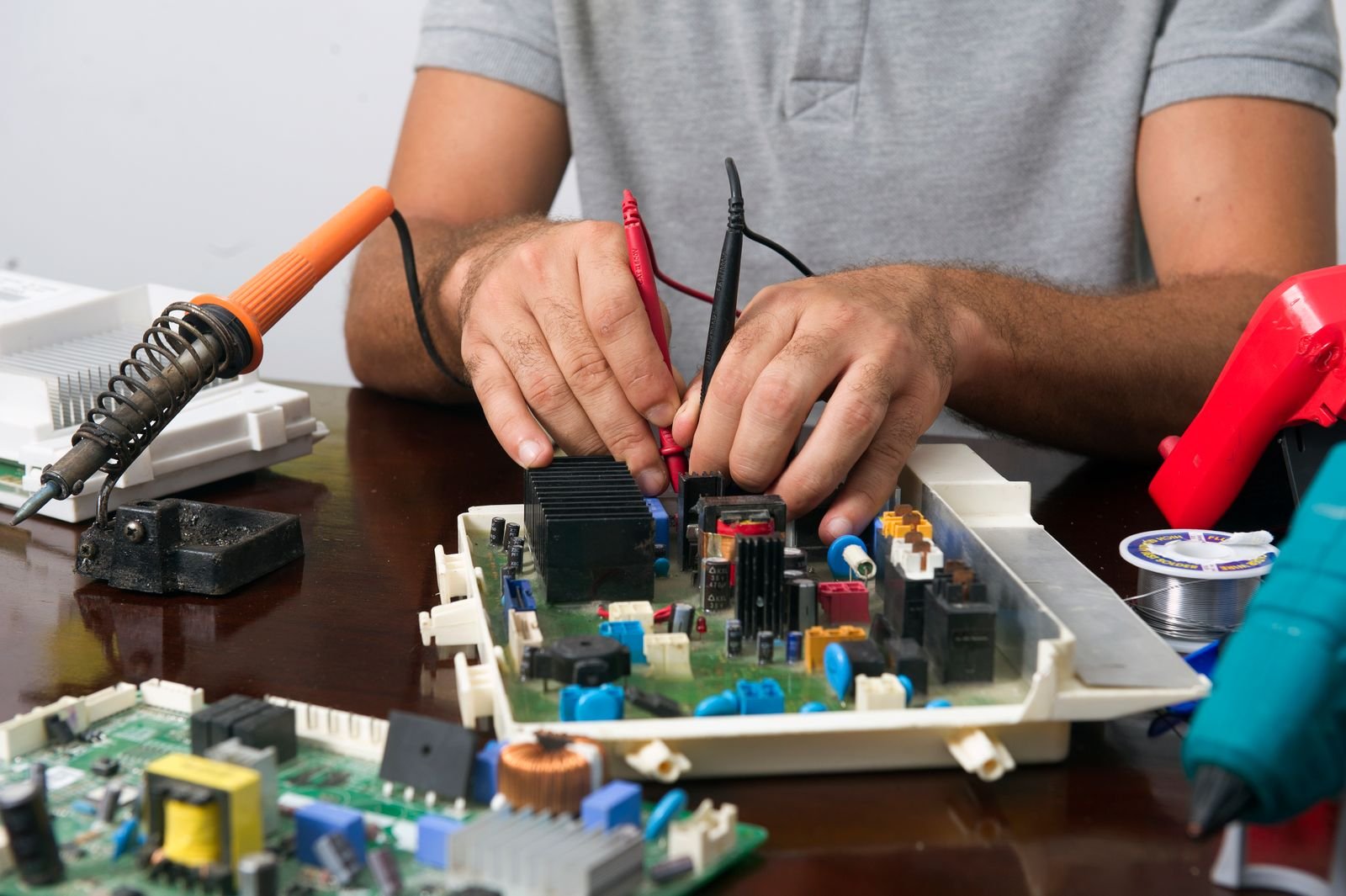 Man working on an electronic circuit board with tools on a table, showing close-up of hands and components