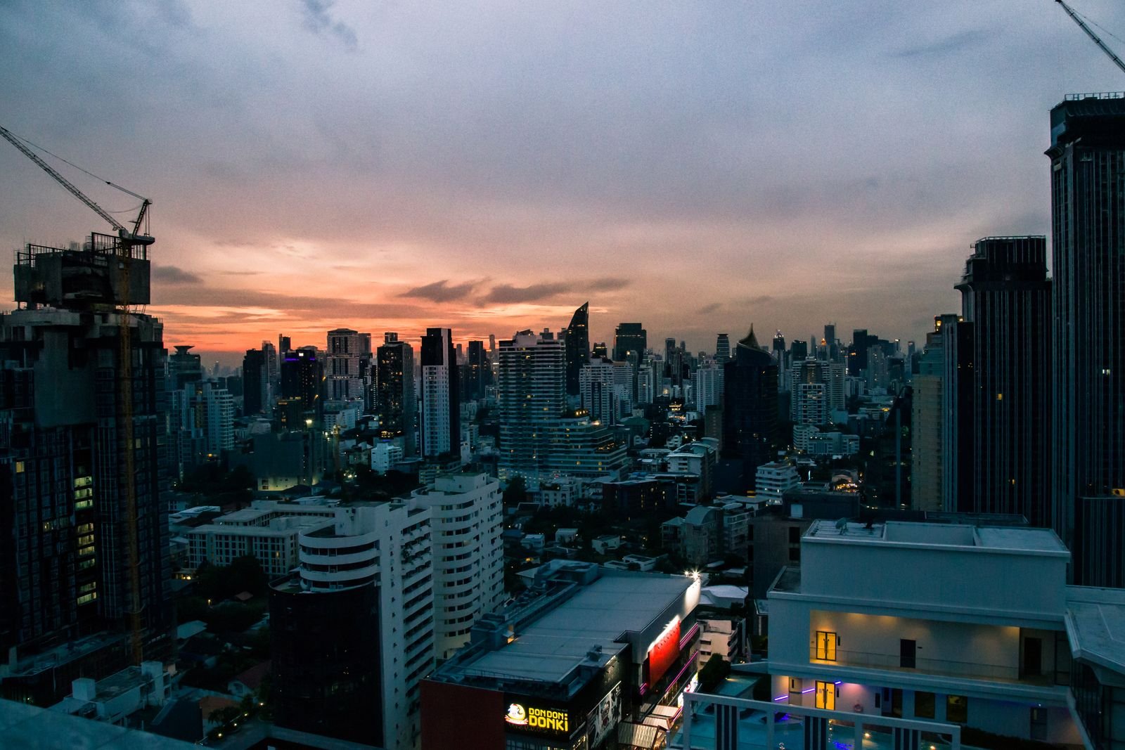 Dramatic urban sunset with skyscrapers and cranes over a bustling city skyline