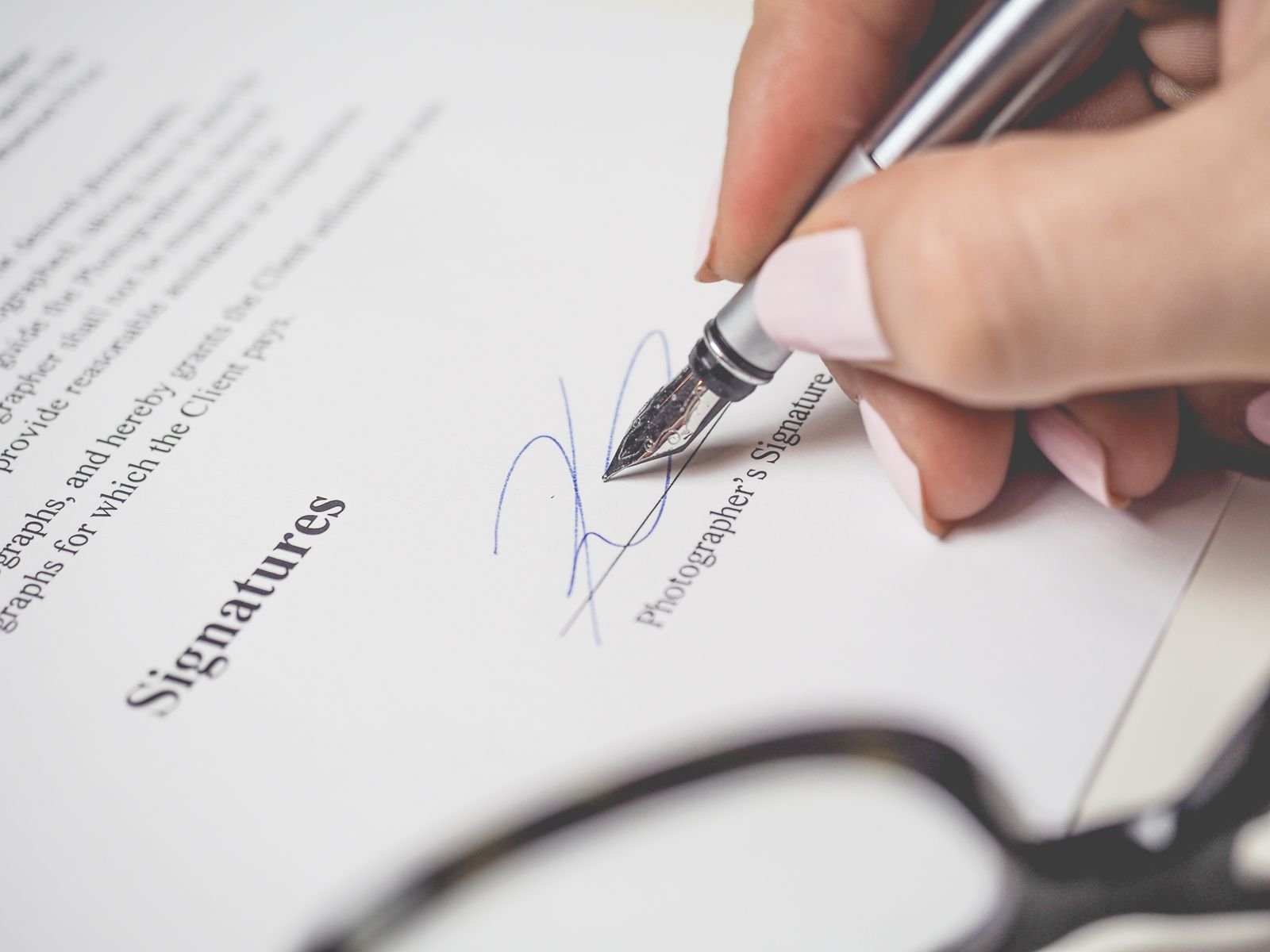 Close-up of a hand signing a contract, showcasing a pen and elegant handwriting