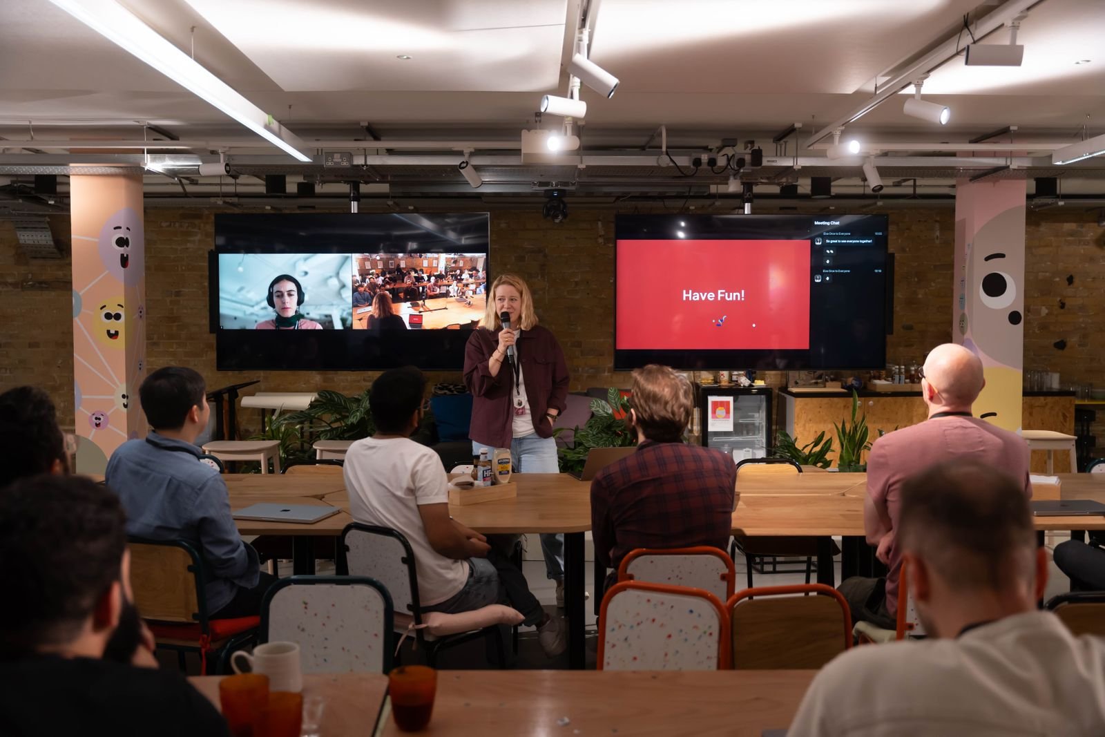 A speaker engages with an audience in a modern conference setup. Interactive screens enhance the presentation