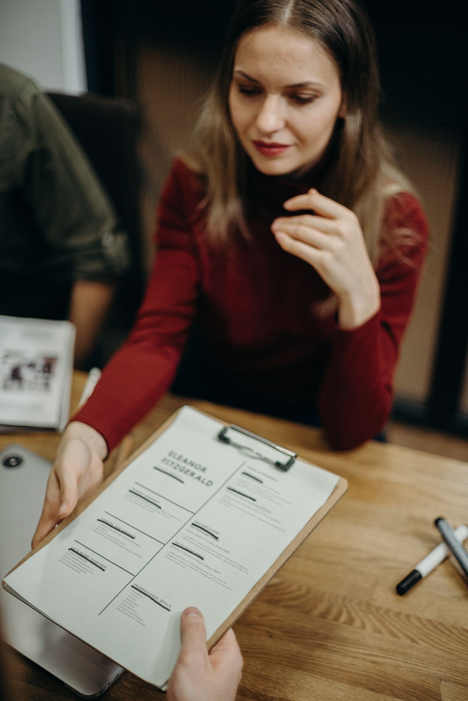 Woman sitting at a desk holding a clipboard and reviewing a resume during a job interview