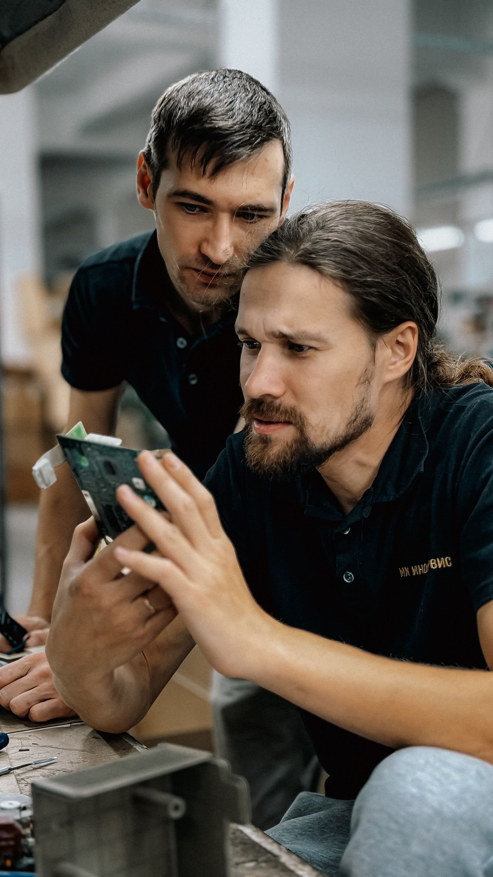Two engineers closely inspecting a green circuit board for electronic components