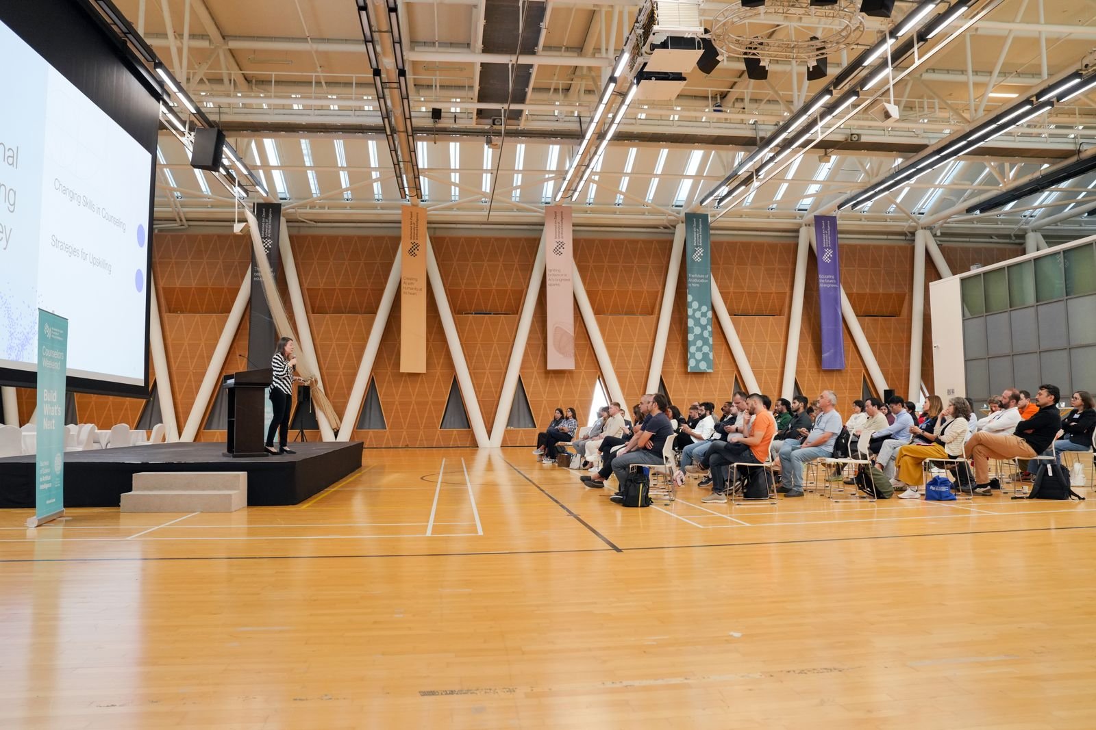 Large indoor conference with audience focused on a speaker presenting from a podium