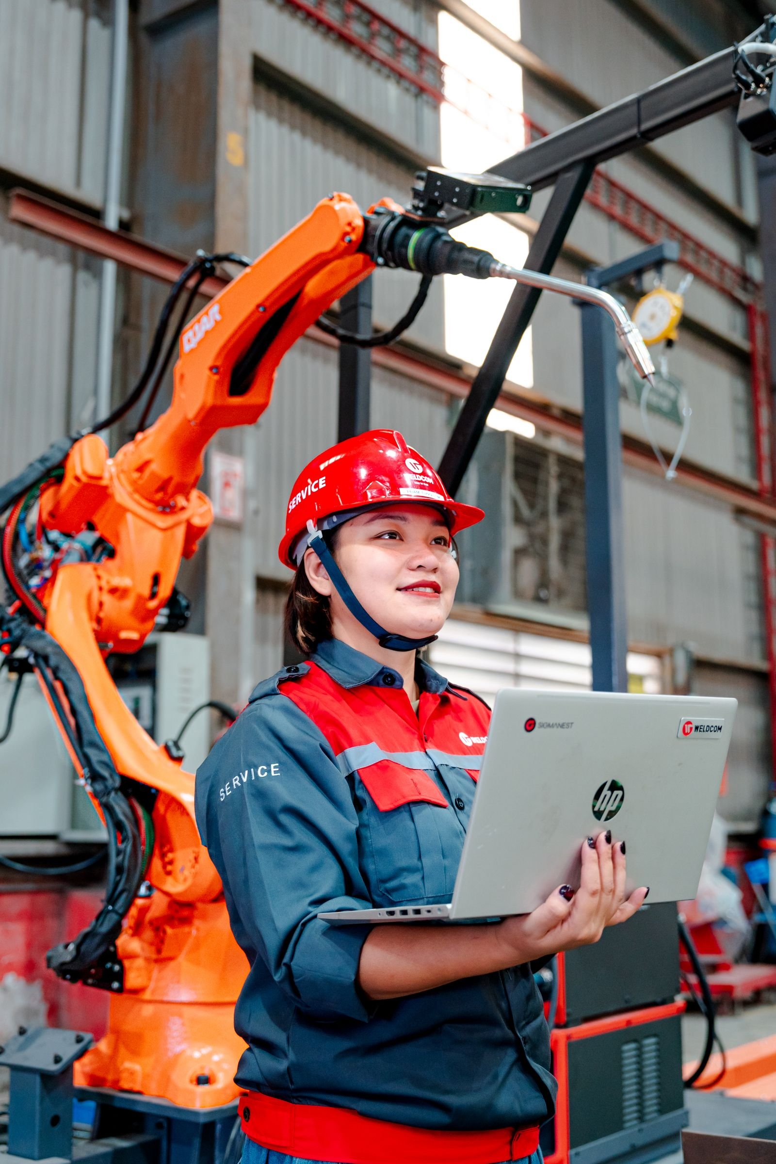 Female engineer with laptop overseeing robotic arm in a manufacturing setting in Vietnam