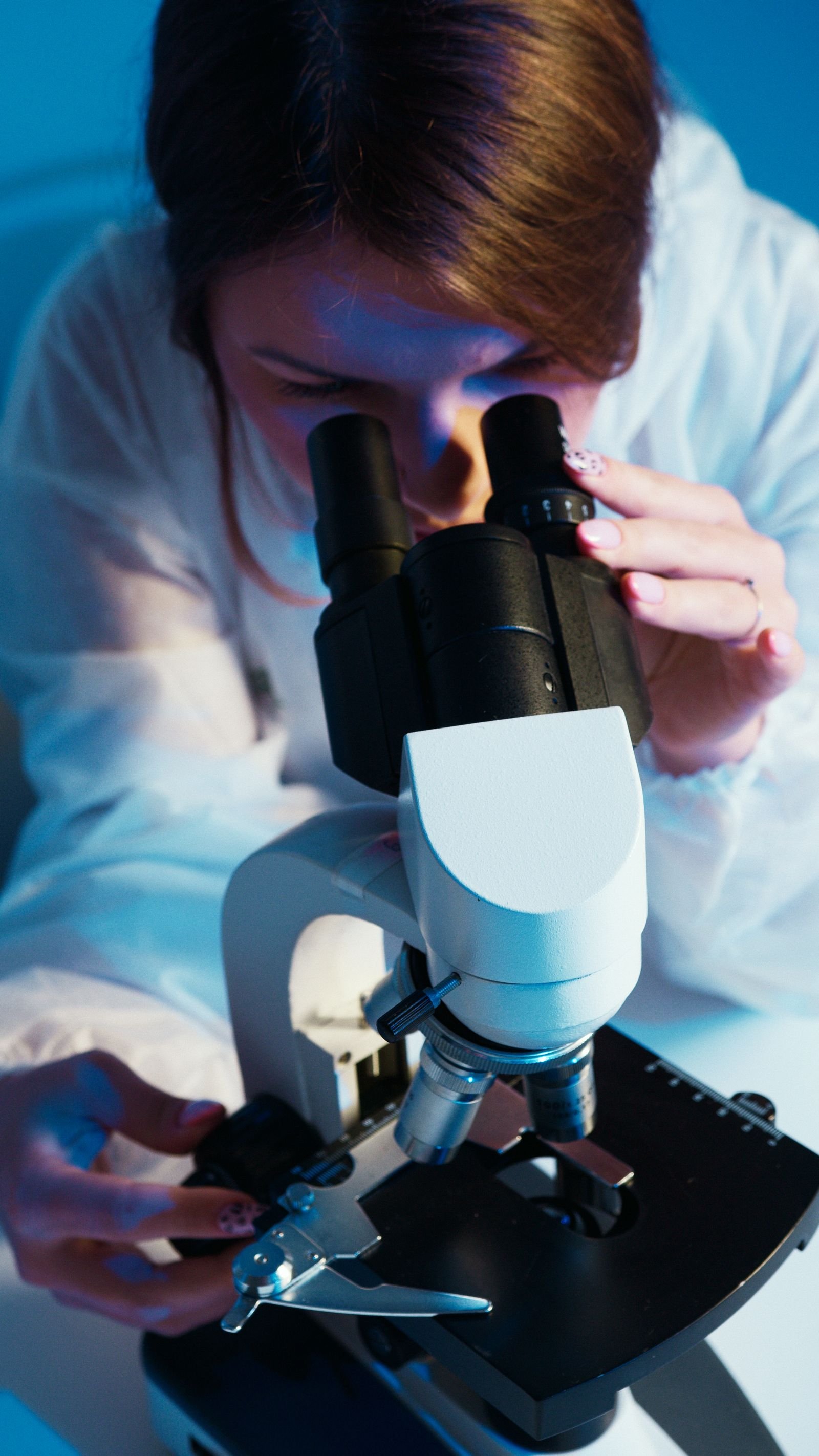 A female scientist wearing protective gear analyzing a sample using a microscope in a laboratory
