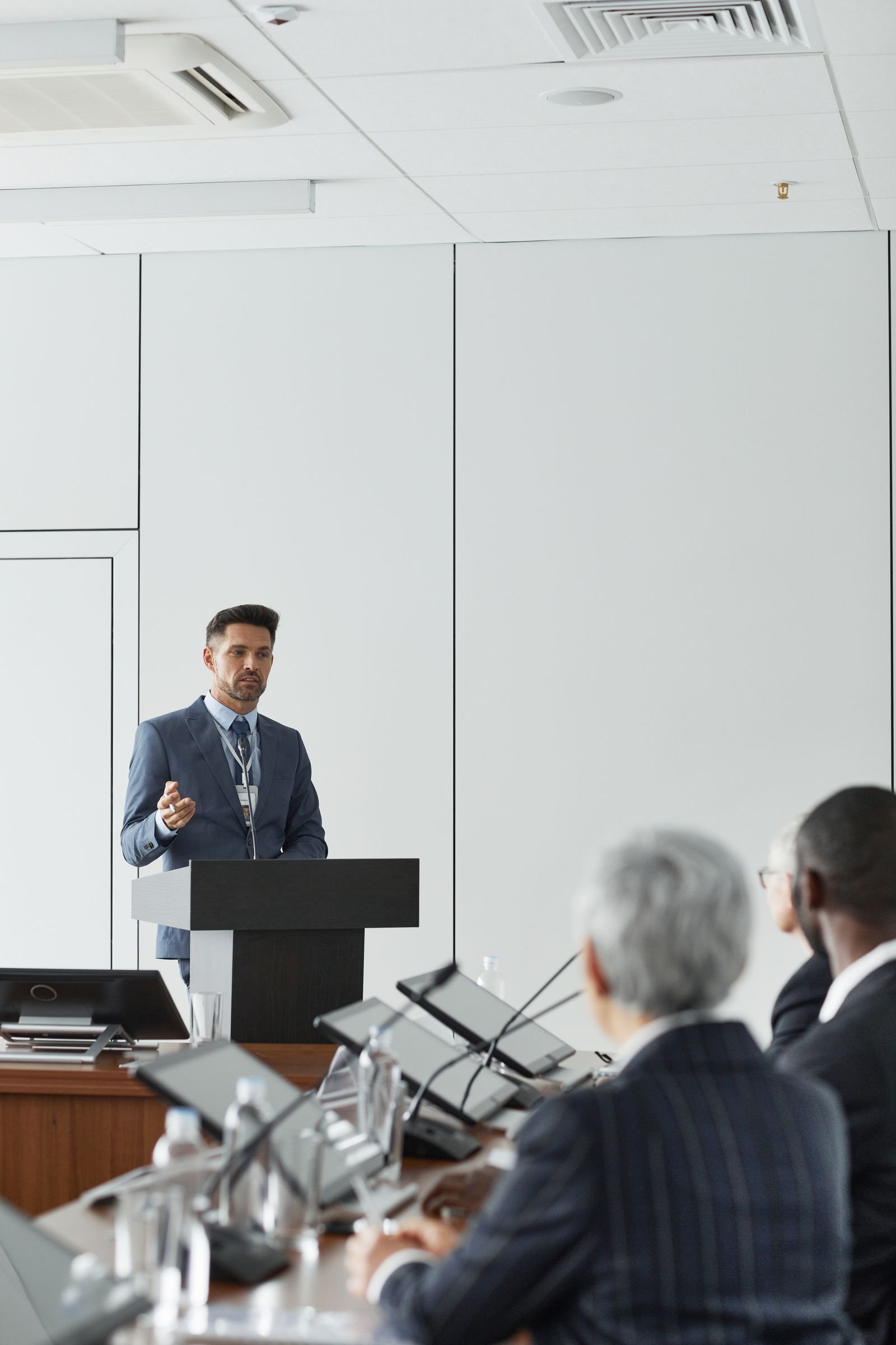 A man in a blue suit giving a presentation at a conference podium indoors