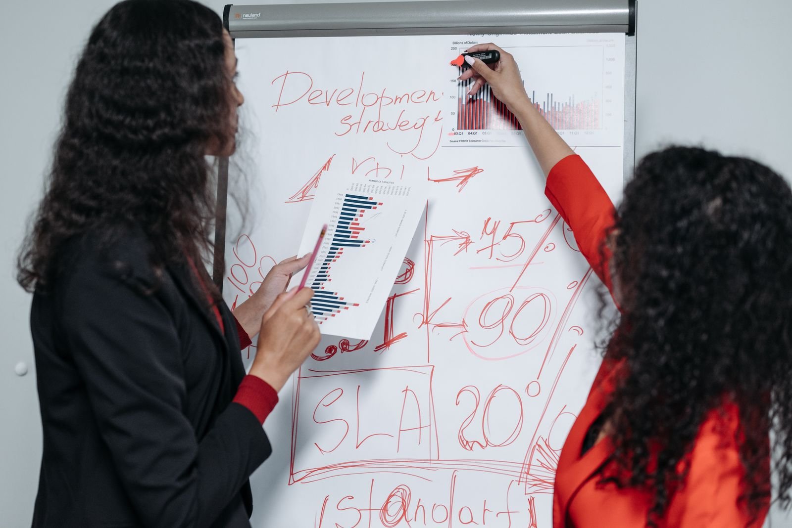 Two professional women discuss and strategize on business development in a modern office setting