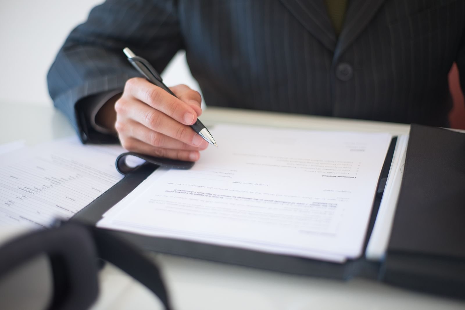 Close-up of a hand signing documents with a pen, symbolizing an important business contract